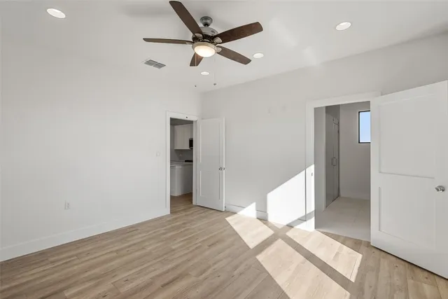 a view of an empty room with wooden floor and a ceiling fan