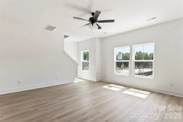 an empty room with wooden floor ceiling fan and kitchen view
