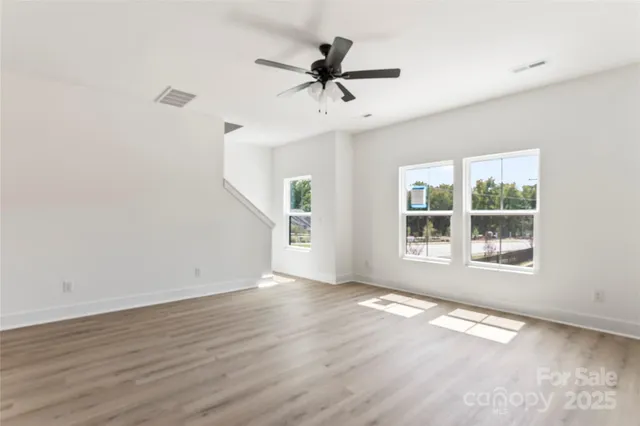 an empty room with wooden floor ceiling fan and kitchen view