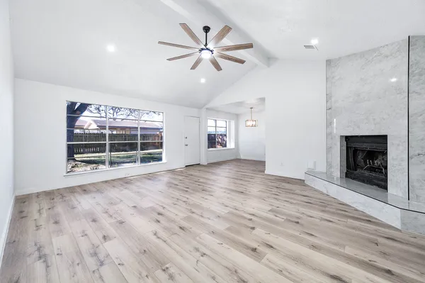 an empty room with wooden floor fireplace and windows