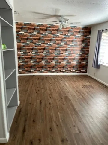 an empty room with wooden floor fan and windows