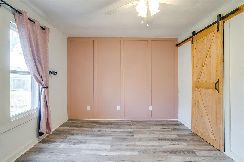 206 Bateman Street Meridian, TX 76665 - Photo 15 of 26 Unfurnished bedroom with a barn door, light wood-style floors, ceiling fan, and a decorative wall