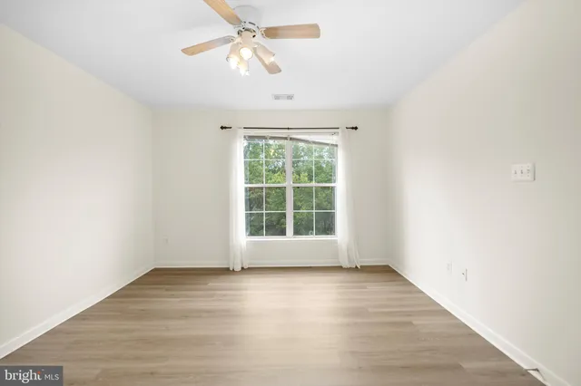 an empty room with wooden floor chandelier fan and windows