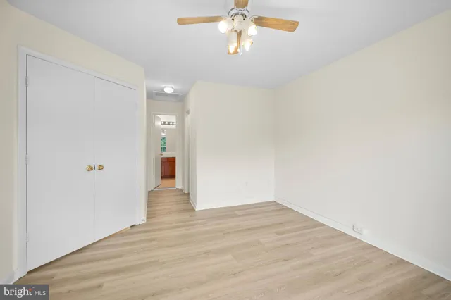 a view of an empty room with wooden floor and a ceiling fan