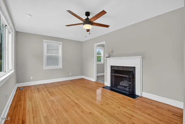 an empty room with wooden floor a ceiling fan a fireplace and windows
