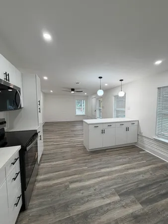 a large white kitchen with kitchen island a sink dishwasher a stove and a refrigerator with wooden floor