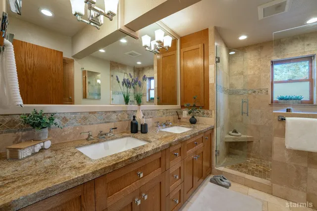 a bathroom with a granite countertop double vanity sink a mirror and a shower