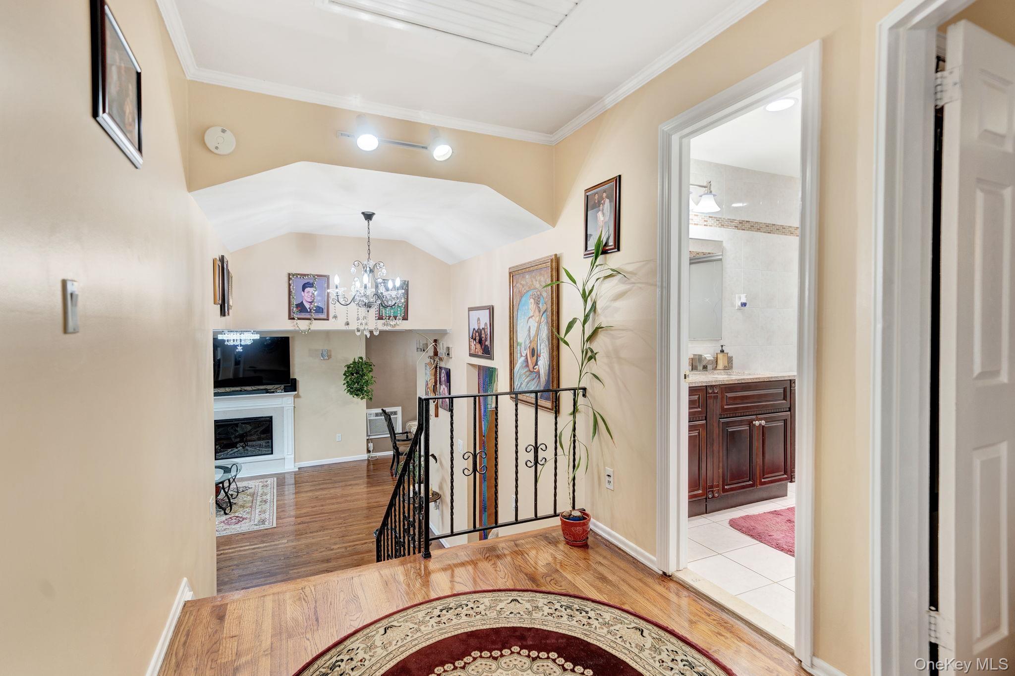 1 Wayland Road Plainview, NY 11803 - Photo 16 of 28 Entryway with light wood-type flooring, a fireplace, a chandelier, crown molding, and vaulted ceiling