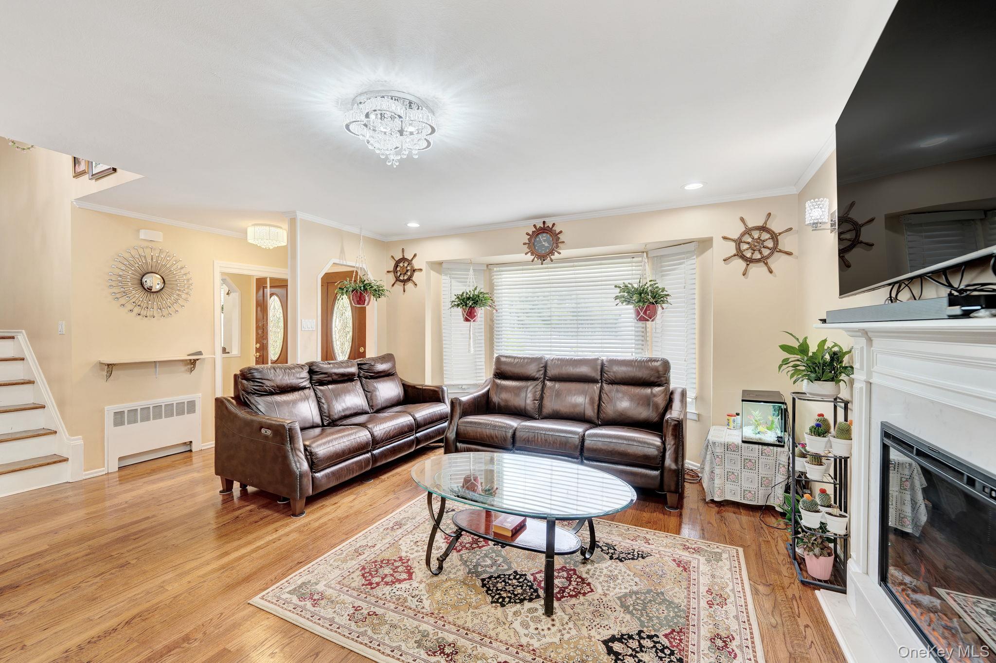 1 Wayland Road Plainview, NY 11803 - Photo 6 of 28 Living area with radiator heating unit, ornamental molding, light wood-style floors, a fireplace with flush hearth, and stairs