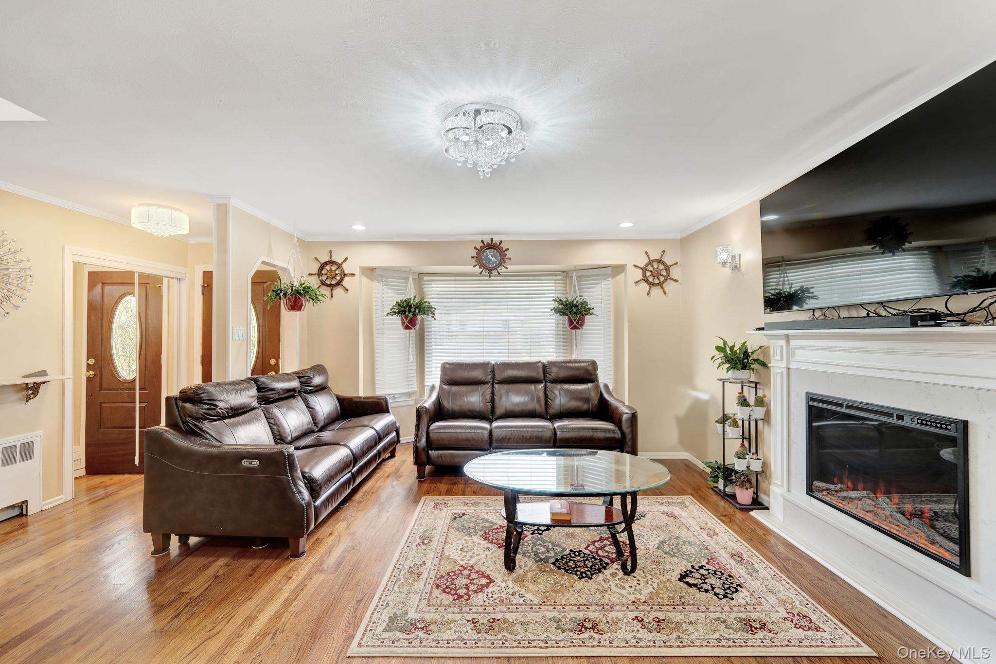 1 Wayland Road Plainview, NY 11803 - Photo 7 of 28 Living room featuring light wood-type flooring, a glass covered fireplace, crown molding, radiator, and recessed lighting