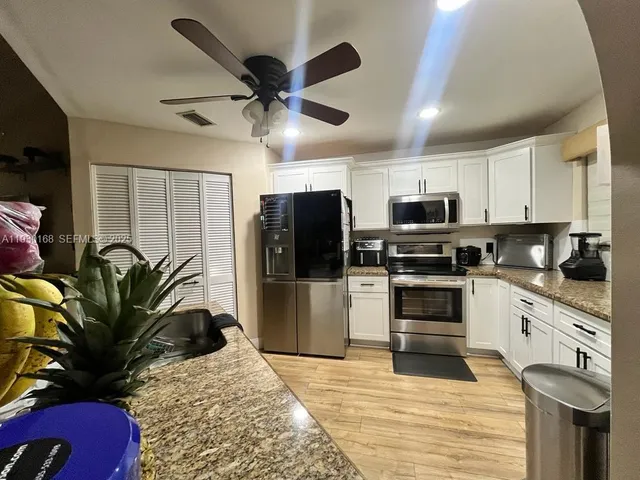 a kitchen with stainless steel appliances kitchen island granite countertop a refrigerator a stove a sink dishwasher and white cabinets with wooden floor
