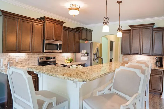 a kitchen with stainless steel appliances granite countertop a sink a stove a refrigerator cabinets a dining table and chairs