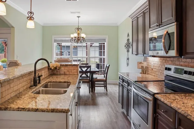 a kitchen with granite countertop a stove a sink a kitchen island with chairs and wooden floor