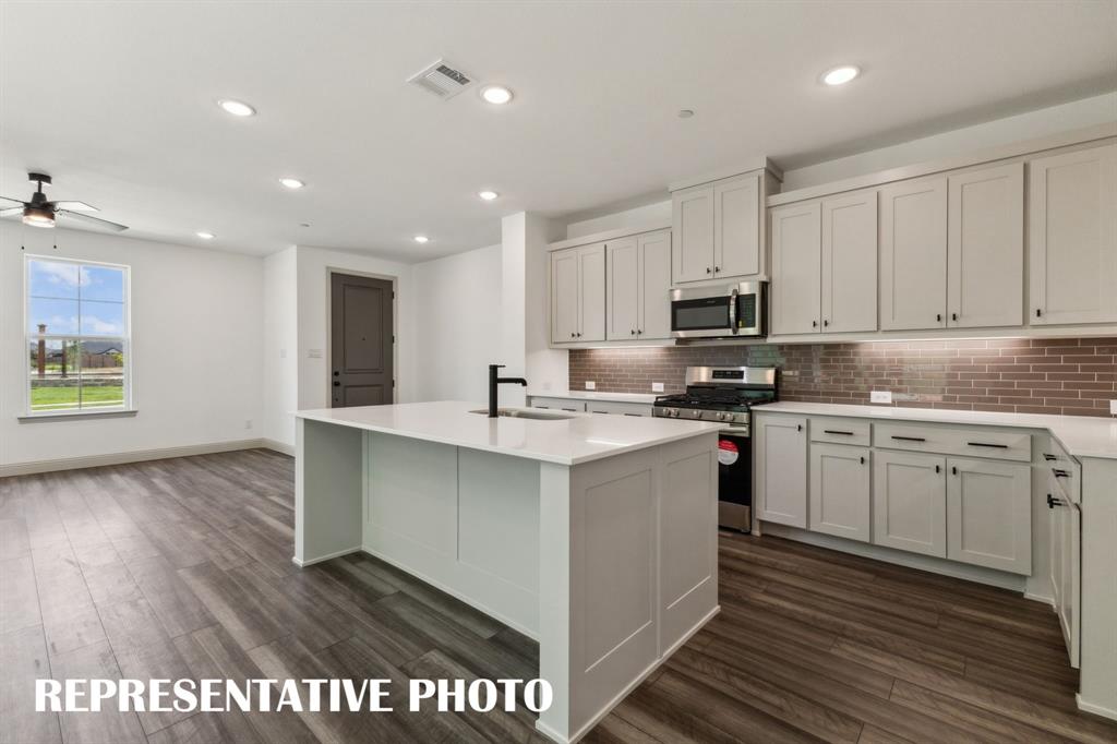 1009 Splitrock Drive Allen, TX 75013 - Photo 6 of 20 a kitchen with stainless steel appliances granite countertop a sink a stove a microwave a sink a refrigerator and white cabinets with wooden floor