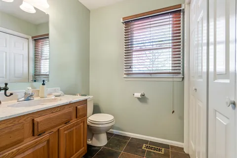 a bathroom with a granite countertop toilet a sink a mirror and a window