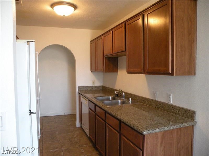 1844 North Decatur Boulevard, Unit 103 Las Vegas, NV 89108 - Photo 5 of 9 Kitchen with brown cabinets, white appliances, arched walkways, dark tile patterned flooring, and dark countertops