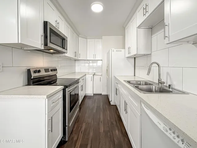 a kitchen with stainless steel appliances granite countertop a sink a stove top oven a refrigerator with white cabinets