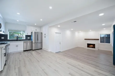 a view of kitchen with stainless steel appliances granite countertop a stove top oven a sink dishwasher a refrigerator and white cabinets with wooden floor