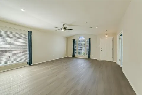 an empty room with wooden floor fan and windows