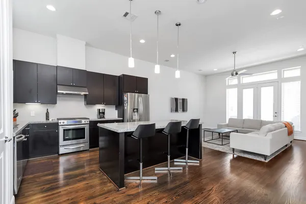 a kitchen with stainless steel appliances kitchen island granite countertop a stove top oven a sink dishwasher a dining table and chairs with wooden floor