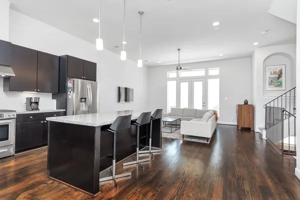 a kitchen with stainless steel appliances granite countertop a refrigerator a sink dishwasher a dining table and chairs with wooden floor