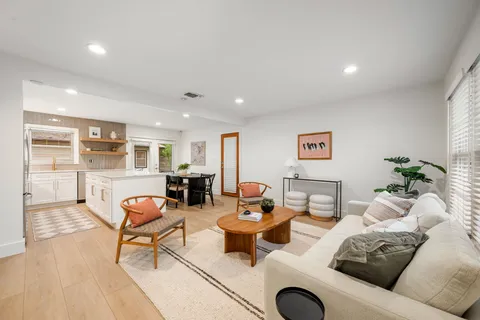 a living room with furniture a rug kitchen view and a large window