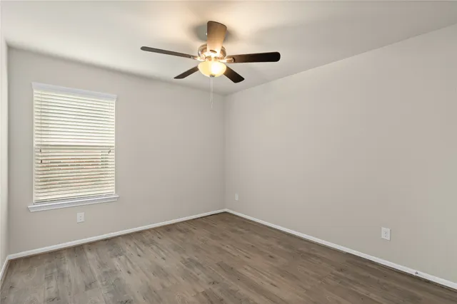 an empty room with wooden floor fan and windows