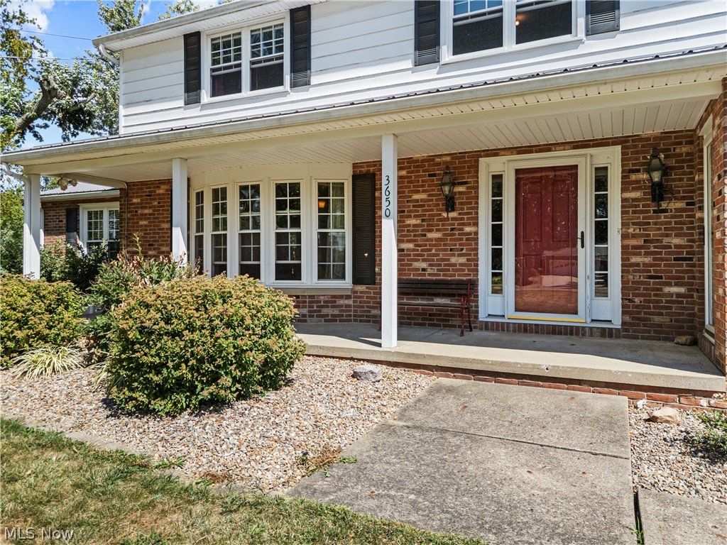 3650 Rambo Avenue Alliance, OH 44601 - Photo 4 of 36 Brick and siding exterior featuring a covered porch, bay window, red entry door, and exterior sconce lighting