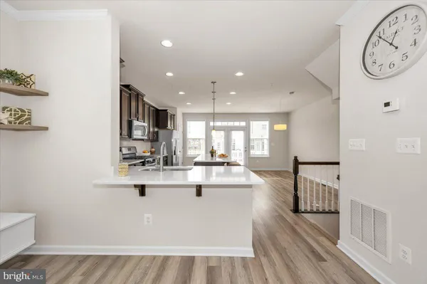 a large white kitchen with kitchen island a stove a refrigerator a sink and a dining table with wooden floor