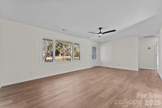 an empty room with wooden floor ceiling fan and windows