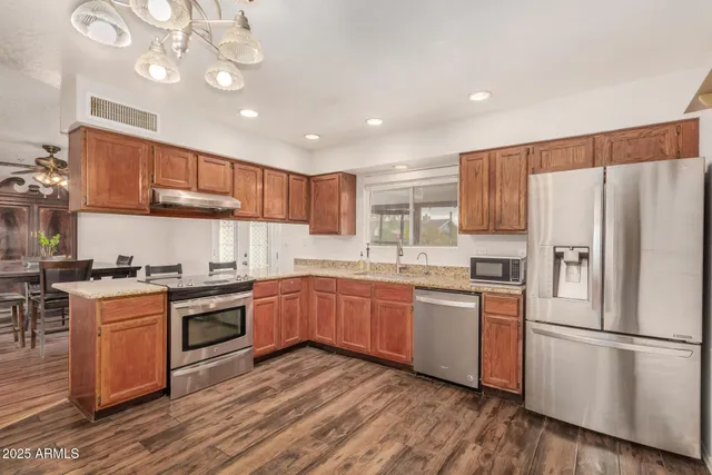 a kitchen with stainless steel appliances granite countertop a refrigerator a stove top oven a sink cabinets and wooden floor