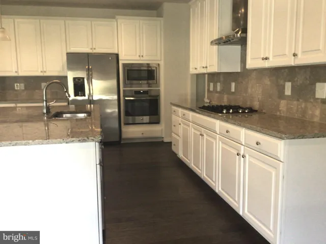 a kitchen with granite countertop a refrigerator a sink and white cabinets