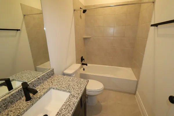 a bathroom with a granite countertop bathtub shower sink vanity and toilet