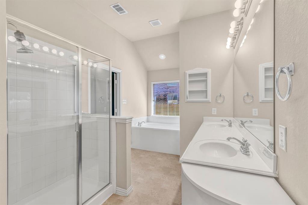 5316 Ridgeson Drive McKinney, TX 75071 - Photo 25 of 33 Bathroom featuring a glass-enclosed shower with white tiled walls, a dual vanity with white countertops and chrome fixtures, a large mirror with overhead lighting, and a built-in corner bathtub