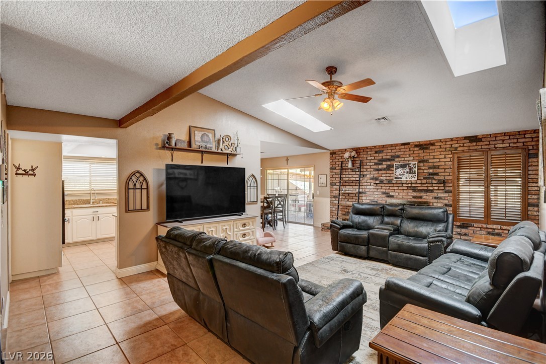 Exposed wood beams and dual skylights crown this tiled living space with a brick accent wall.