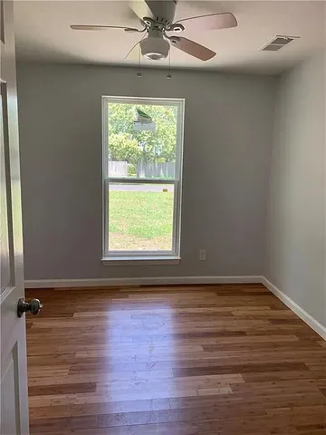 an empty room with wooden floor fan and windows