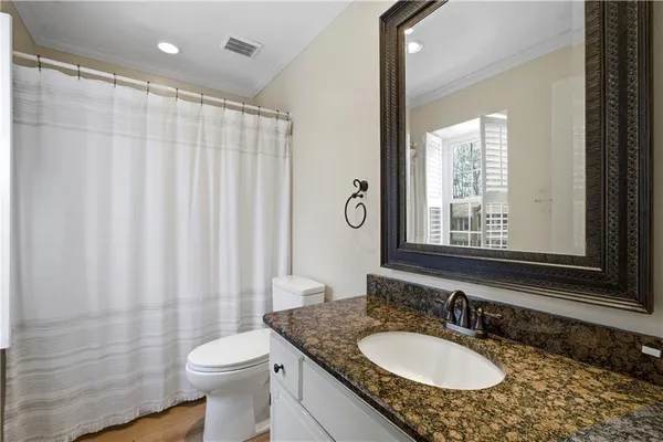 a bathroom with a granite countertop sink a toilet a mirror and shower curtain