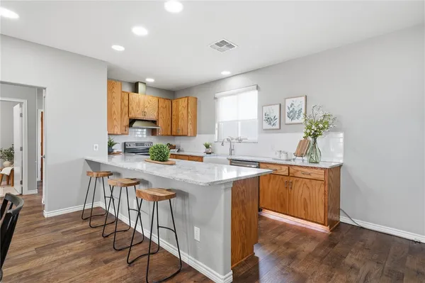 a kitchen with stainless steel appliances granite countertop wooden cabinets a sink a stove a dining table and chairs