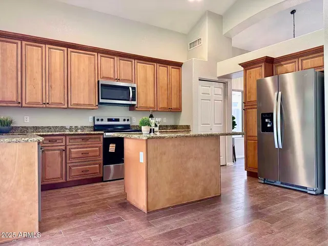 a kitchen with stainless steel appliances granite countertop a refrigerator stove and a sink with wooden floors