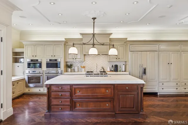 a large kitchen with kitchen island granite countertop a stove a sink a refrigerator and white cabinets with wooden floor