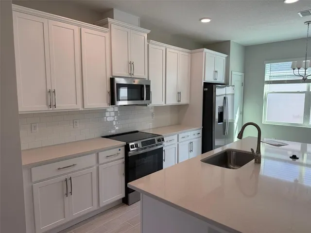 a kitchen with stainless steel appliances a sink a stove a refrigerator with white cabinets