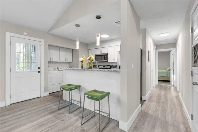 a kitchen with stainless steel appliances granite countertop a refrigerator a microwave oven a sink dishwasher and white cabinets with wooden floor