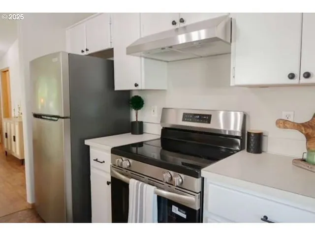 a kitchen with stainless steel appliances kitchen island granite countertop a refrigerator a stove a sink dishwasher and white cabinets with wooden floor