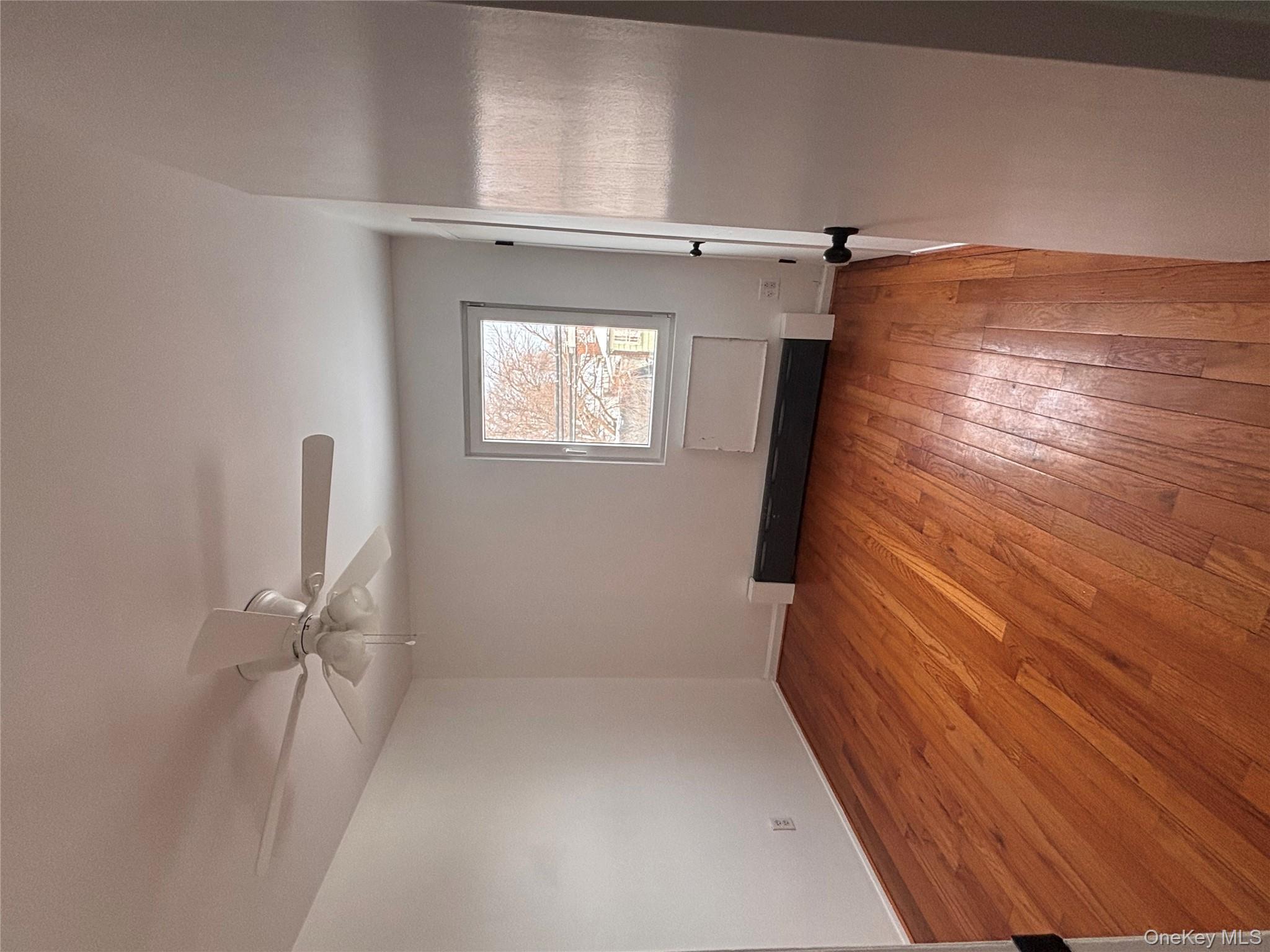 145-01 223rd Street, Unit 2 Queens, NY 11413 - Photo 12 of 12 an empty room with wooden floor fan and windows