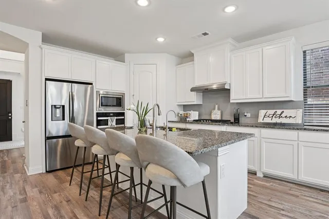 a kitchen with stainless steel appliances granite countertop a stove a sink a refrigerator and white cabinets with wooden floor