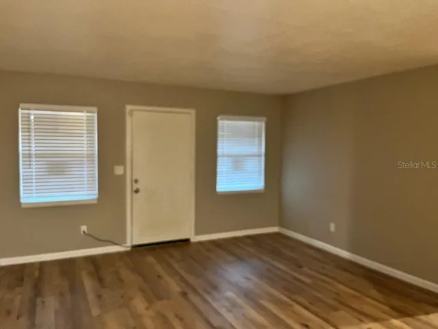 a view of an empty room with wooden floor and a window