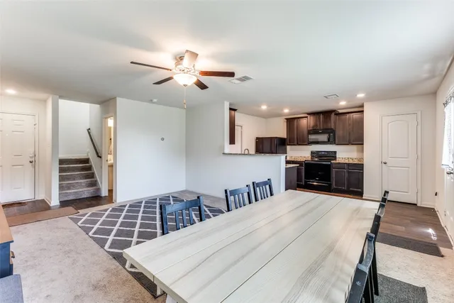 a kitchen with stainless steel appliances kitchen island granite countertop a stove top oven a sink a dining table and chairs with wooden floor