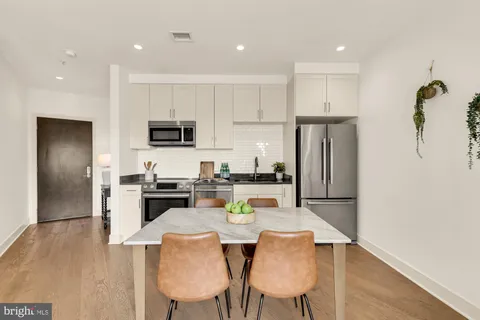 a kitchen with stainless steel appliances granite countertop a refrigerator a stove a sink a dining table and chairs with wooden floor