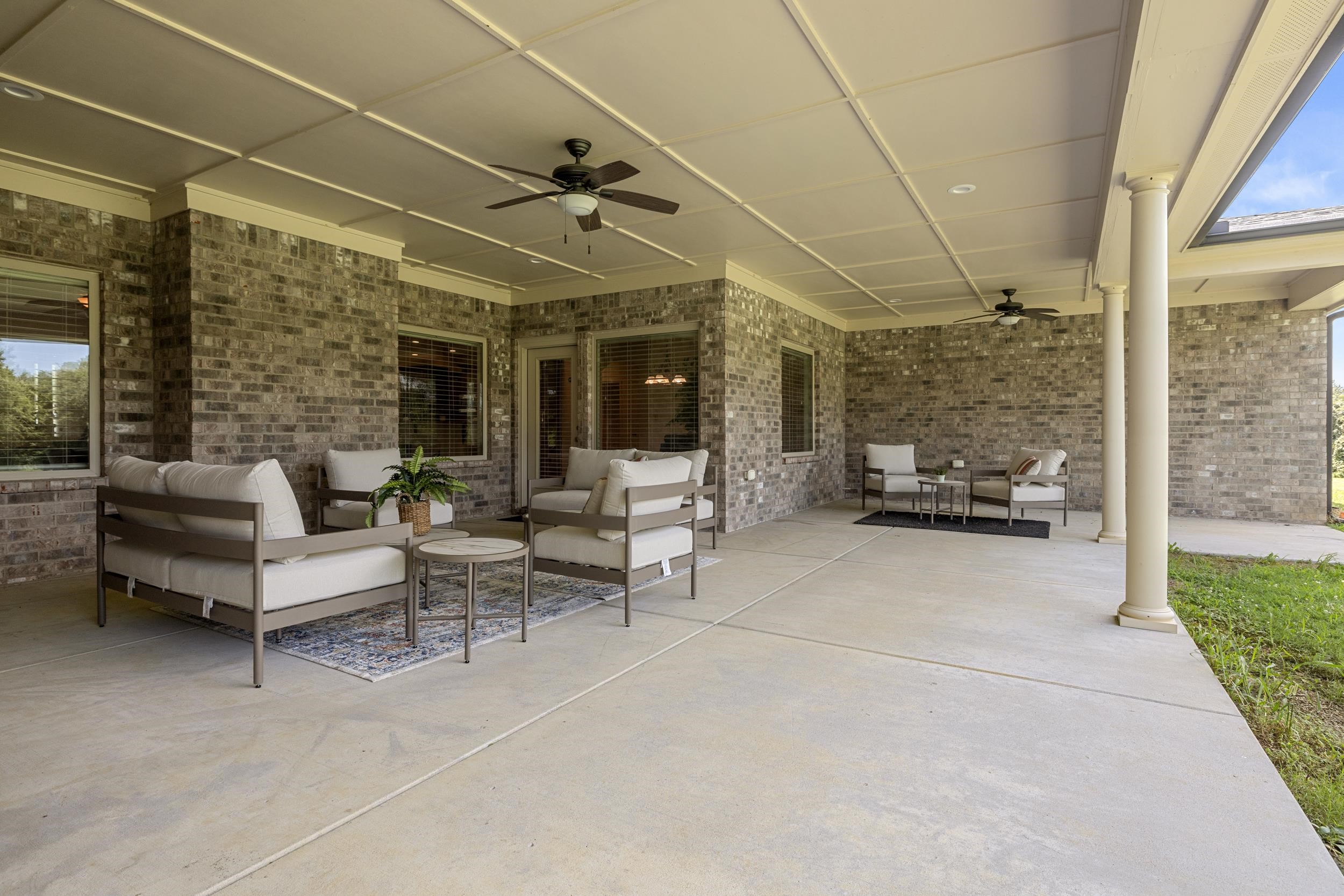 185 Belmont Road Mason, TN 38049 - Photo 6 of 38 Expansive covered patio featuring a coffered ceiling, two ceiling fans, substantial brick exterior, multiple windows with blinds, and durable concrete flooring