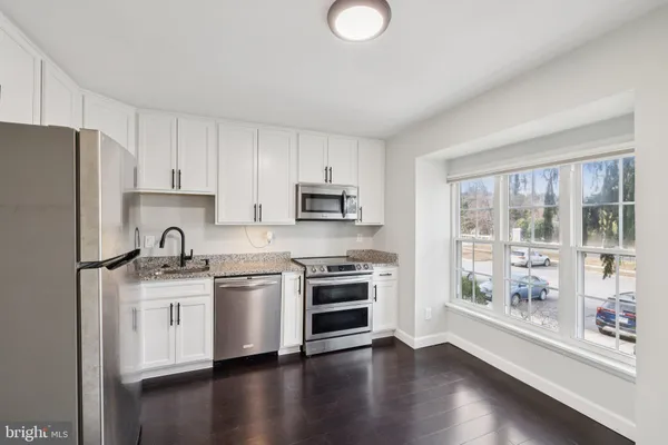 a kitchen with stainless steel appliances granite countertop a stove top oven a refrigerator a sink and a granite counter tops with wooden floors